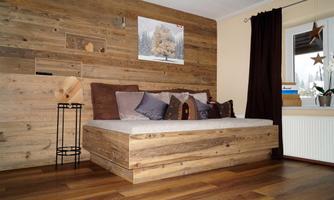 A cozy room with wooden walls and a modern bed. The windows let in a lot of light, and the decor is simple and inviting.