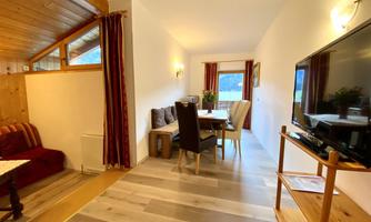 A cozy holiday apartment with wood paneling and a dining area. The bright living room is modernly furnished and offers a view outside.