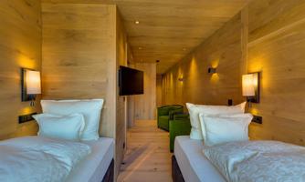 A modern bedroom with two beds and warm wooden paneling. The room features subdued lighting and cozy furniture.
