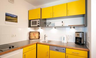 A modern kitchen with yellow cabinets and an elegant countertop. It features basic appliances such as a microwave, kettle, and coffee maker.