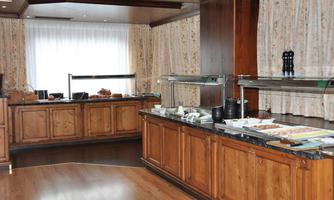 An inviting breakfast area with wooden cabinets and white curtains. Various foods and drinks are displayed on the buffet.