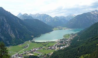 A breathtaking landscape with mountains and a clear lake. In the foreground lies a small village surrounded by green meadows.