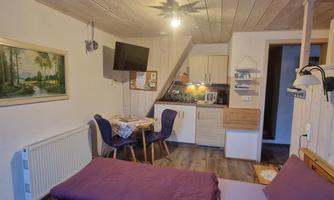 A cozy holiday apartment with a double bed, a small dining area, and a kitchenette. The wooden ceilings give the room a warm atmosphere.