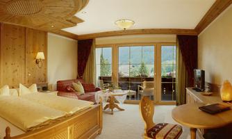 A spacious hotel room with a traditional wooden ceiling and cozy décor. Large windows offer a view of the beautiful landscape.