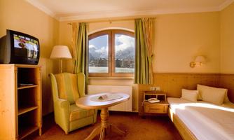 A cozy hotel room with a TV, a table, and an armchair. A beautiful mountain landscape is visible through the window.