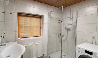 A modern bathroom with a shower and a washing machine. The room has a bright, friendly atmosphere due to the ceiling lighting and the window.