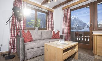 A cozy living area with a gray sofa and red cushions. Through the window, there is a view of the mountains and the beautiful landscape.