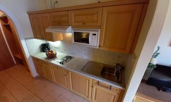 A modern kitchen with wooden cabinets, a stove, and a microwave. Fresh fruits and a coffee machine are visible on the countertop.