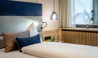 A modern bedroom with a cozy bed and a stylish headboard. The room has large windows with a view of the mountains and a bright, inviting atmosphere.