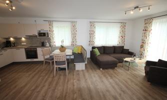 A modern apartment with an open kitchen and a comfortable living area. Bright windows and floral curtains give the room an inviting atmosphere.