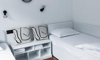A modern bedroom with two single beds and a minimalist design. A decorative bicycle hangs on the wall, and cushions are placed on the bench.