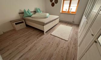 A modern bedroom with a large bed and green pillows. The bright walls and wooden floor create a cozy atmosphere.