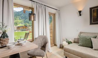 A cozy room with a bright sofa and a table decorated with dishes. Through the window, there is a view of a beautiful mountain landscape.