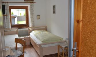 A simple bedroom with two beds and a window looking outside. The walls are bright, and the decor is modern and minimalistic.