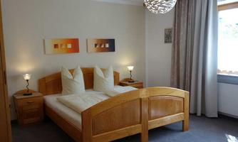 A bright bedroom with a large bed and two pillows. Decorative pictures are on the walls and the window lets in plenty of daylight.