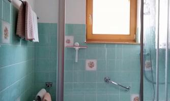 A bathroom with a bathtub and a shower cabin. The walls are covered in light green tiles, and there is a window that lets in natural light.