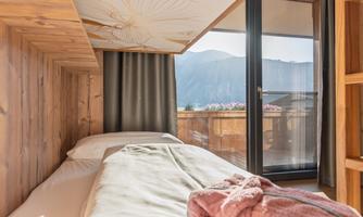 A modern bedroom with wooden paneling and a view of the mountains. Large windows let in plenty of light and provide access to a balcony.