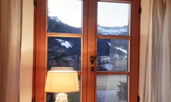 A cozy window with a wooden frame overlooking snow-capped mountains. A lamp sits on the windowsill, providing warm light.