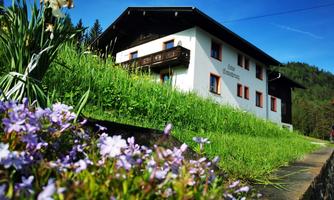 A beautiful house surrounded by green grass and colorful flowers. The sky is clear and blue.