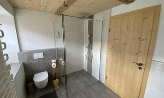 A modern bathroom with a glass shower and a wooden door. The walls are bright, and the furnishings are simple and elegant.