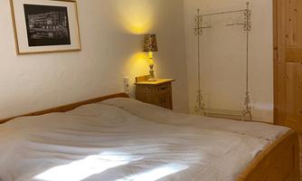 A cozy bedroom with a large wooden bed and soft light. A picture hangs on the wall and there is a metal clothes rack.