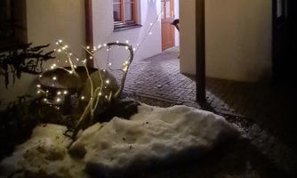 A cozy entrance door at night, illuminated by lights. Snow lies in the foreground and the surroundings appear inviting.
