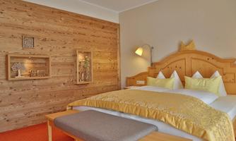 A cozy room with wooden paneling and warm colors. The bed is decorated with yellow pillows and a blanket, and there is a small seating area.