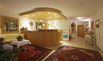 An inviting reception area with a wooden counter and warm lighting. The room is cozy decorated and has a carpet as well as plants.