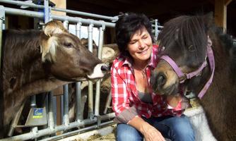A woman is sitting next to a small pony and a cow. Both animals are looking at her curiously.