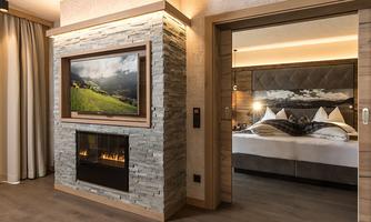 A modern hotel room with a television above an elegant stone fireplace. In the background, a comfortable bed with stylish pillows can be seen.