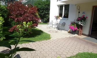 A cozy garden with a paved area and several chairs. Colorful flowers and green grass surround the house.
