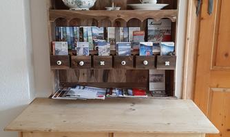 A wooden shelf with postcard compartments and dishes. Below is a table with a drawer.