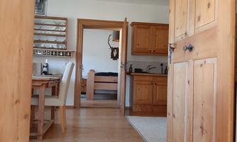A cozy interior with beautiful wooden furniture. In the background, a kitchen and a bedroom are visible.