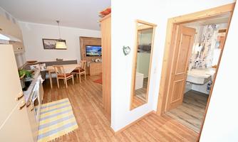 A bright and modern kitchen with a dining area and wood details. In the background, there is access to a bathroom and a mirror on the wall.