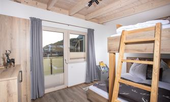 A cozy room with a bunk bed and wooden furniture. Large windows provide plenty of daylight and a view of the outdoors.