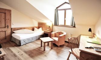 A cozy room with a double bed, a seating area, and a desk. Large windows provide plenty of daylight.