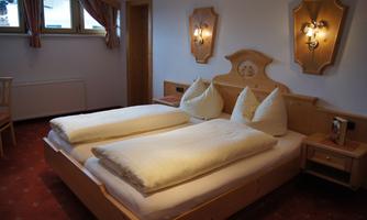 A cozy bedroom with two single beds and large pillows. The walls are bright and illuminated with warm light.