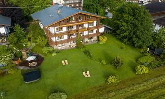 A cozy house with a large garden and lots of greenery. In the garden, there are loungers and a trampoline.