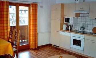 A bright and cozy kitchen with a wooden floor and yellow curtains. The room is modernly furnished with a dining area and a balcony.
