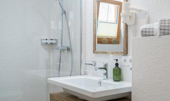 A modern bathroom with a shower cabin and a sink. The space is bright and elegant with a large mirror and wooden details.