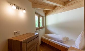 A simple bedroom with wooden shelves and a single bed. The room has a window and warm, natural lighting.