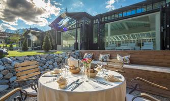 An elegant outdoor table setting with a beautiful view of the surroundings. The table is adorned with dinnerware and decorations, surrounded by modern architecture.