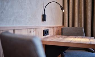 A cozy table with two chairs in a room with wooden paneling. On the wall, there is a small light fixture and electrical outlets.