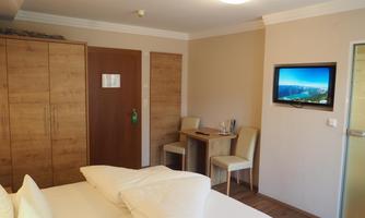 A cozy room with a double bed and wood-colored furniture. There is a small table, chairs, and a television on the wall.