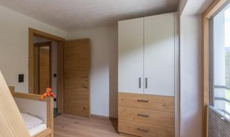 A bright room with a modern wardrobe and a window. In the foreground, there is a bed with a small stuffed animal.