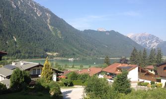 A picturesque landscape with mountains and a clear lake. In the foreground are some houses and a lot of greenery.