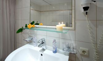 A modern bathroom with a white sink and a mirror. On the sink, there are a candle and fresh flowers.