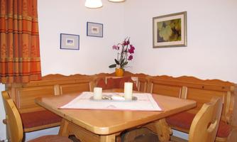 A cozy dining area with a wooden table and bench. On the table are candles and a flower, the walls are decorated with pictures.