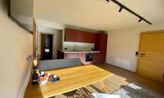 A modern kitchen with a dining table and chairs. The walls are light and there are wooden details in the furnishings.
