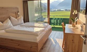 A modern bedroom with a large window and beautiful views of the mountains. The room is friendly and invitingly furnished.